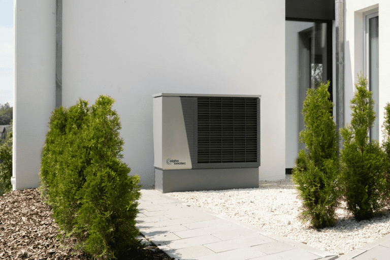 Heat pump amongst white pebbles and greenery.