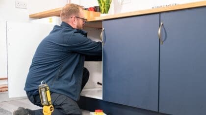 A man is pictured installing technology in a cupboard under the sink.