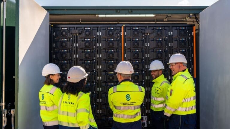 A picture of five members of staff wearing high vis jackets with the Statera Energy logo on the back, looking at a control cabinet.