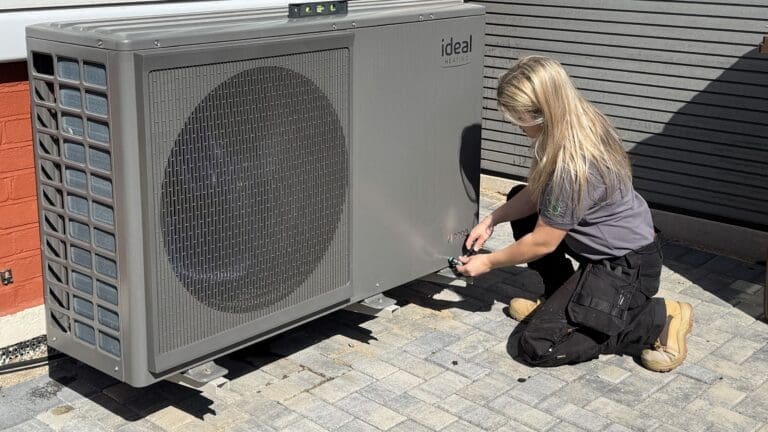 A female installer crouches down next to an Ideal Heating heat pump.